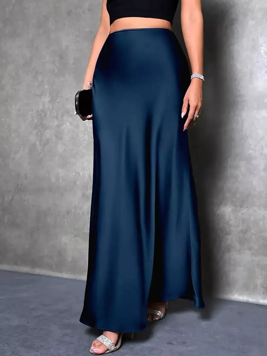 Women's maxi skirt in peacock blue, high waisted satin-look with trumpet hem, holding a clutch