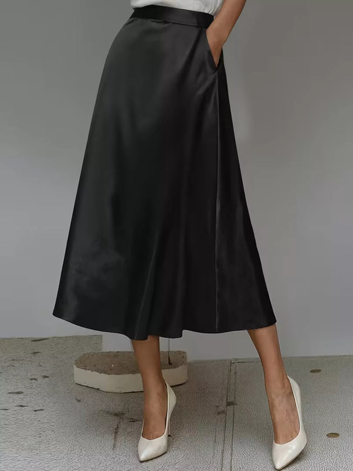 Side angle of the black satin look midi skirt with a hand in the pocket