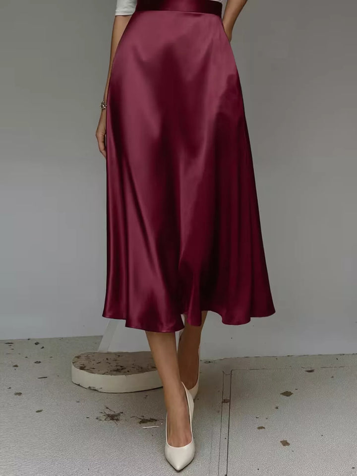 Burgundy satin look midi skirt in a full front view with cream pumps