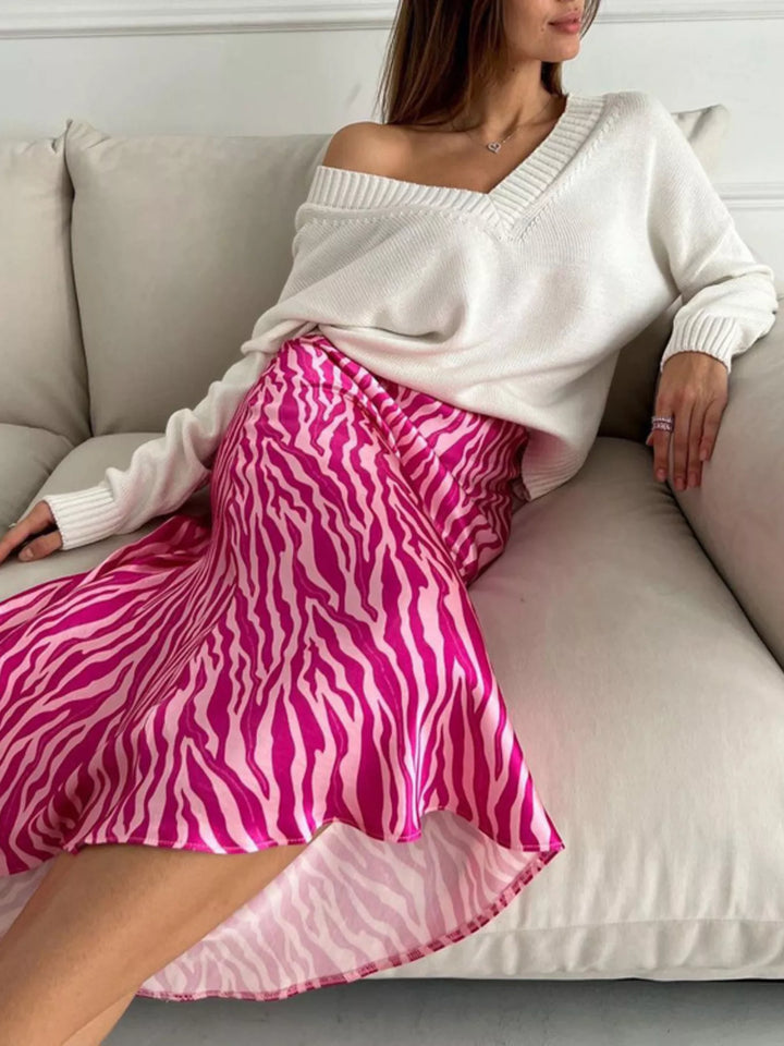 Women's midi skirt in hot pink, satin-look zebra print with flared hem, seated on a sofa