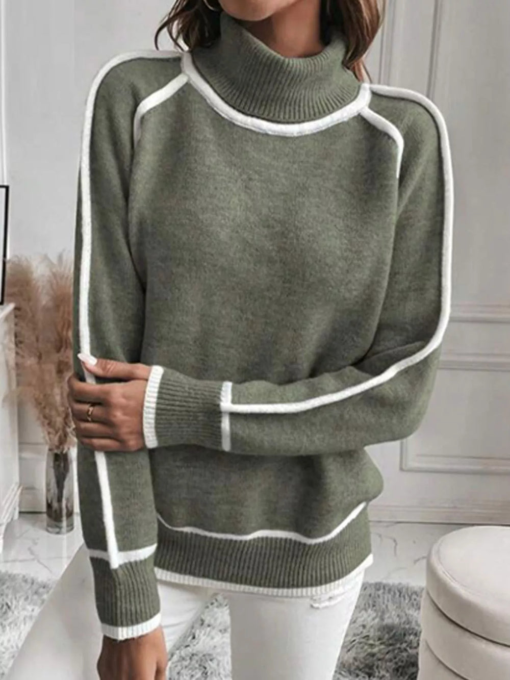 Olive mock neck sweater with white piping, arm crossed over the front