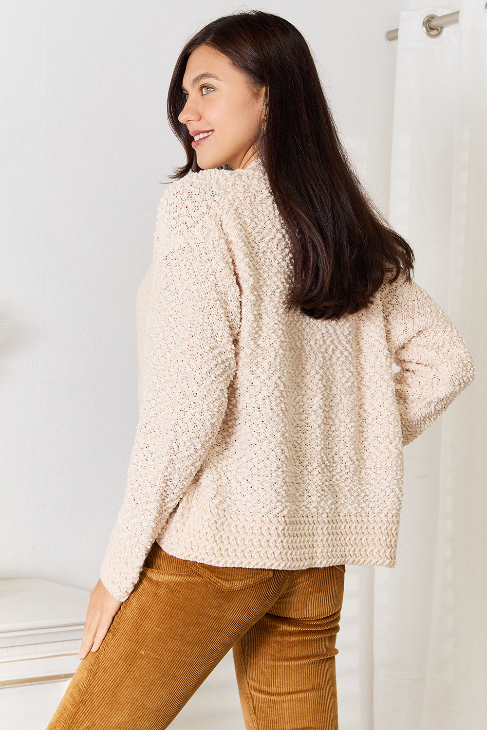 Back view of the cream cropped cardigan as the model looks over her shoulder
