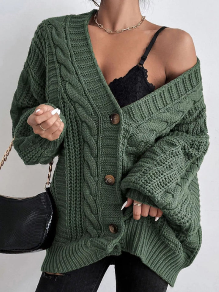 Women's oversized cardigan in forest green, cable knit V neck with balloon sleeves, holding a bag