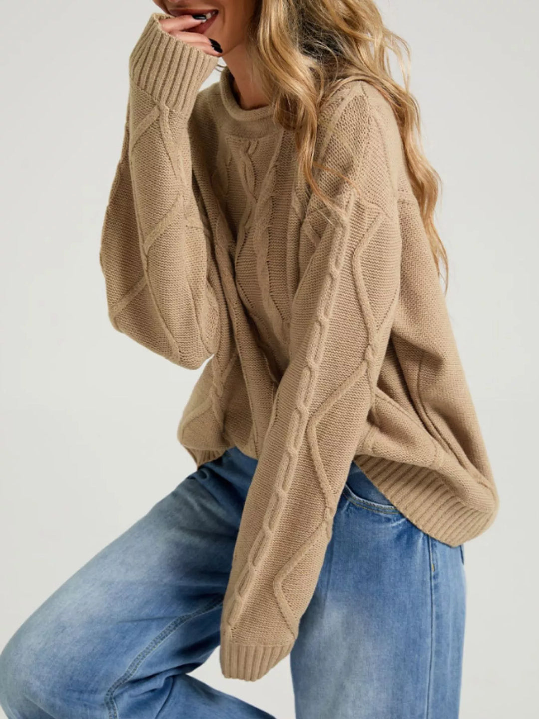 Tan oversized sweater with long sleeves, seated side pose in wide leg jeans