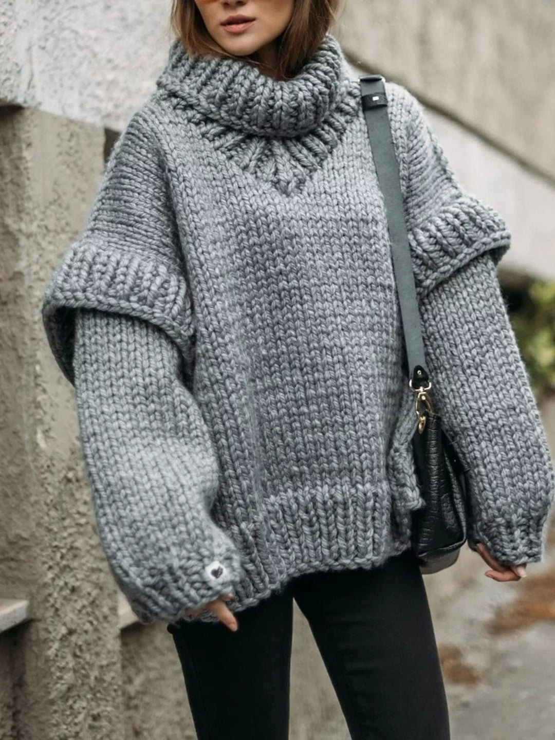 Gray oversized turtleneck sweater with layered shoulders, worn with black pants