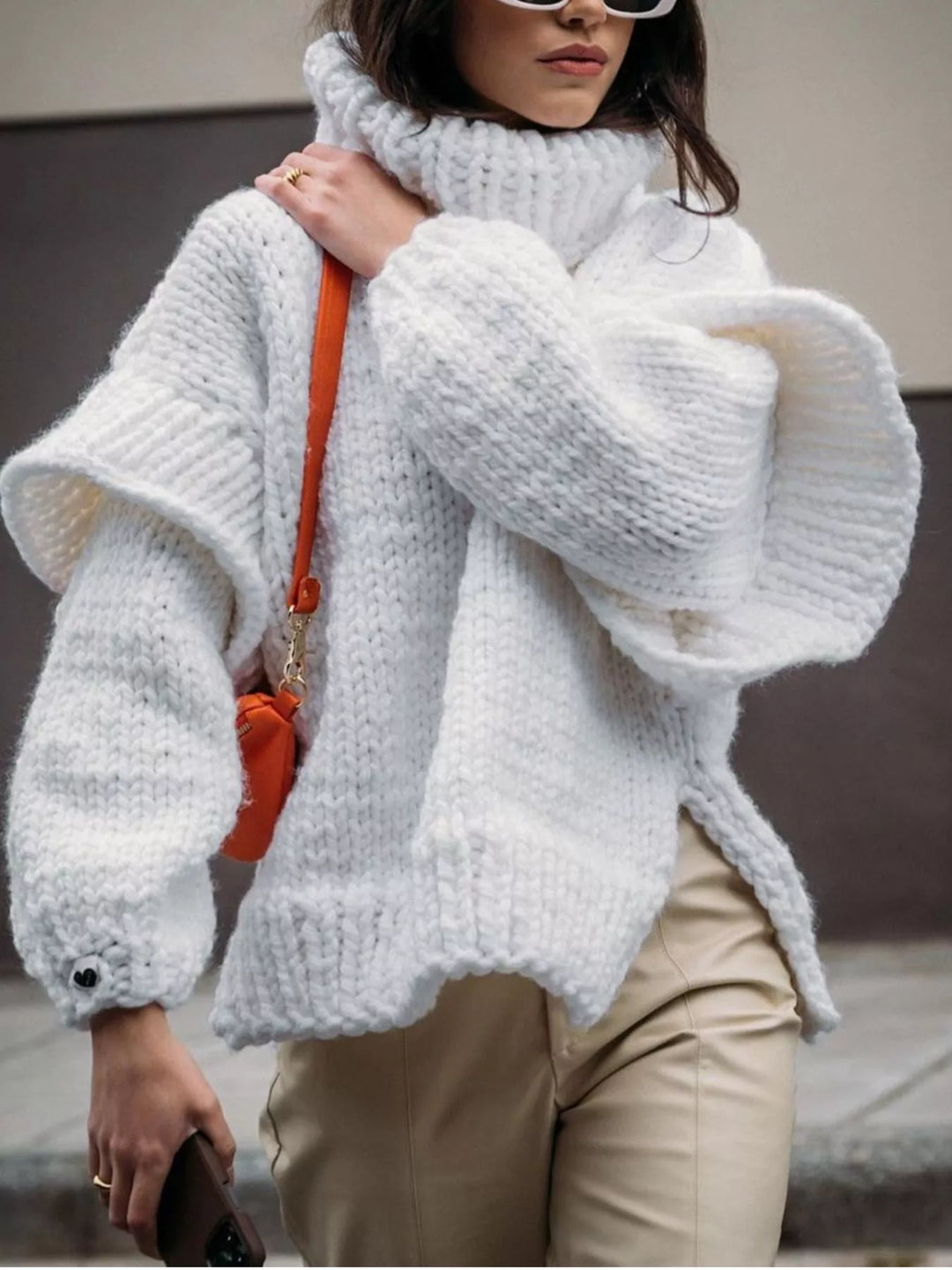 White chunky turtleneck sweater with wide sleeves and a small orange bag