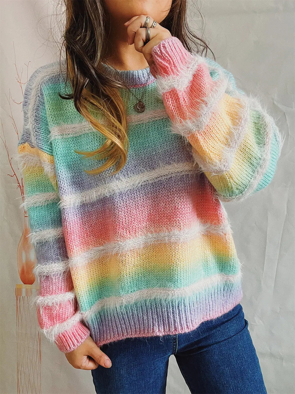 Pastel multicolor striped sweater worn with jeans, hand raised to the face