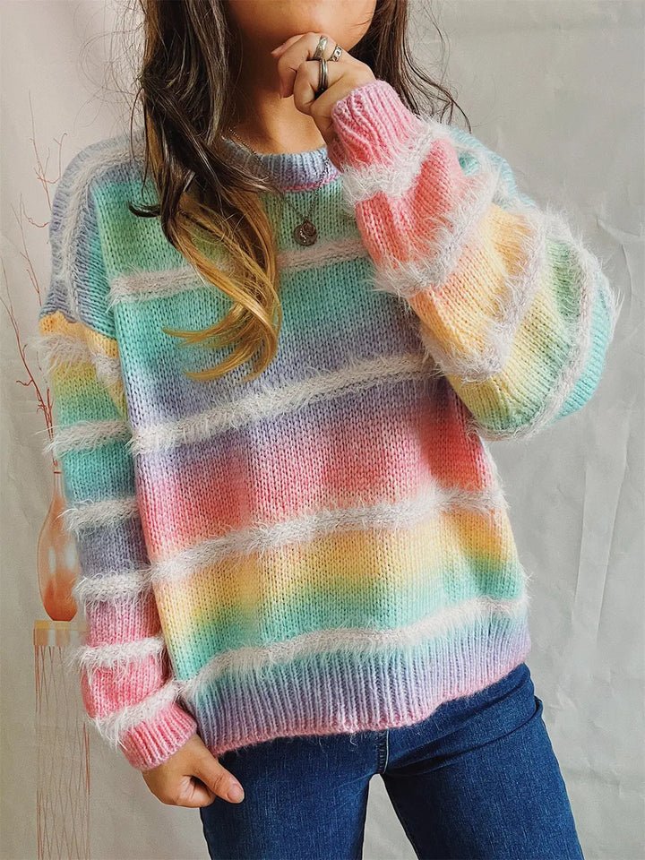Pastel multicolor striped sweater worn with jeans, hand raised to the face