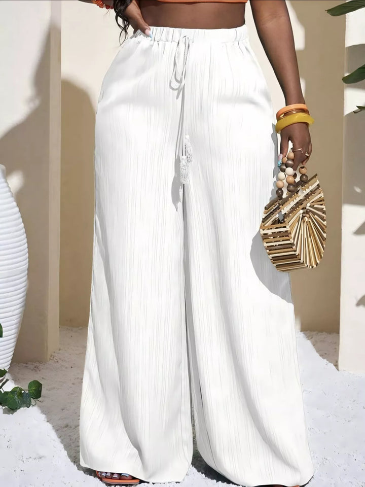 White palazzo pants with tassel drawstring, held with a woven bag