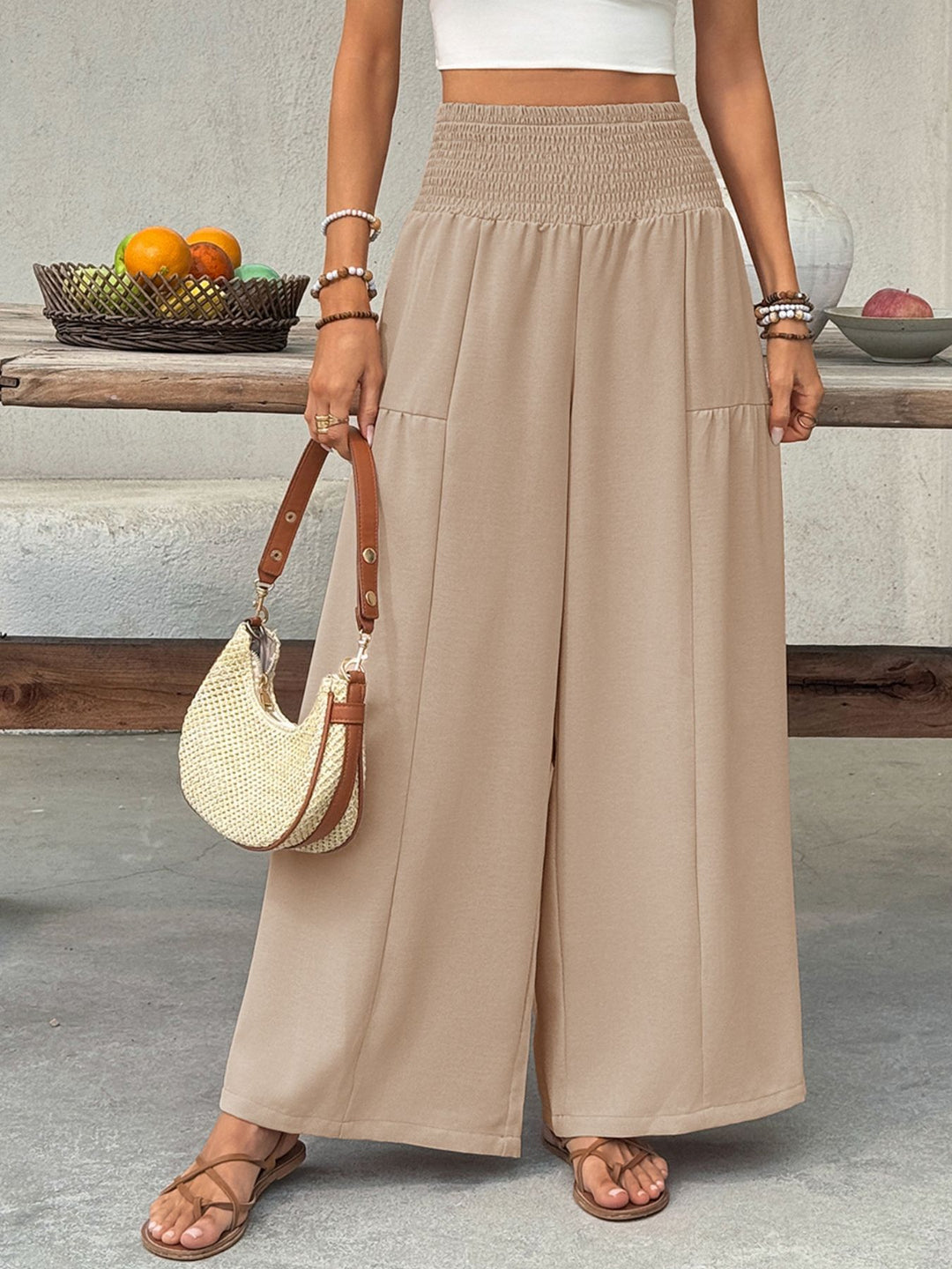 Tan very wide leg pants with a cream shoulder bag and strappy sandals