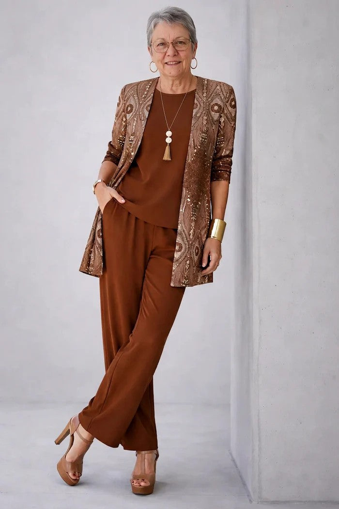 Rust top and pants under a shimmering feather print cardigan, leaning on a wall