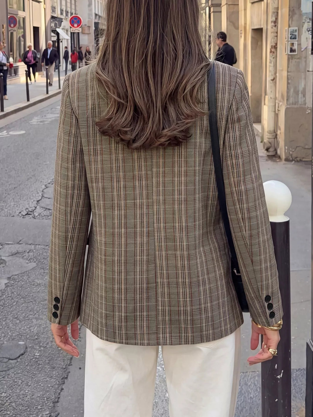 Back view of the mocha plaid blazer with a shoulder bag strap, street setting
