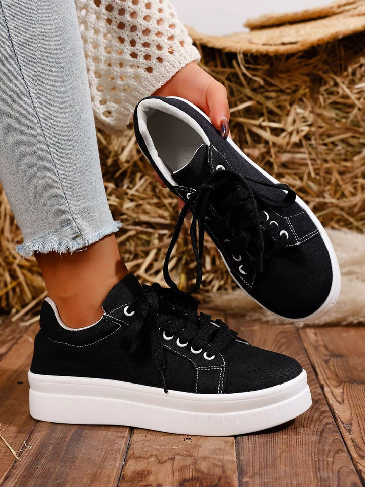 Black chunky sole platform sneakers, one worn and one held, with frayed jeans