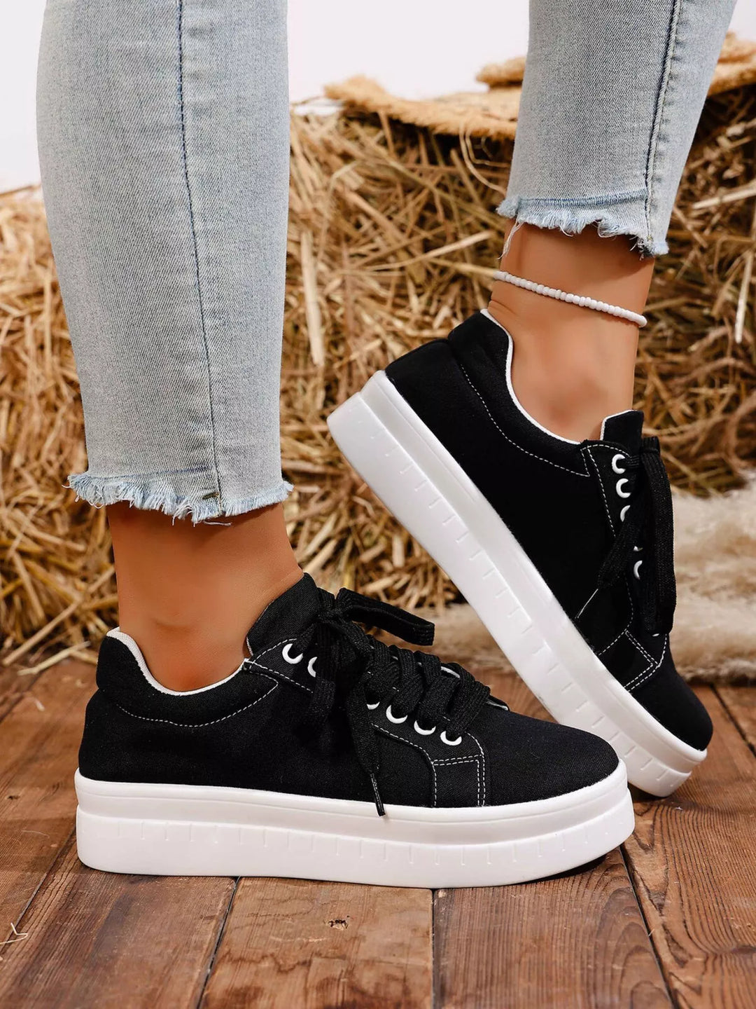 Black low top lace up platform sneakers on a wood floor, side view