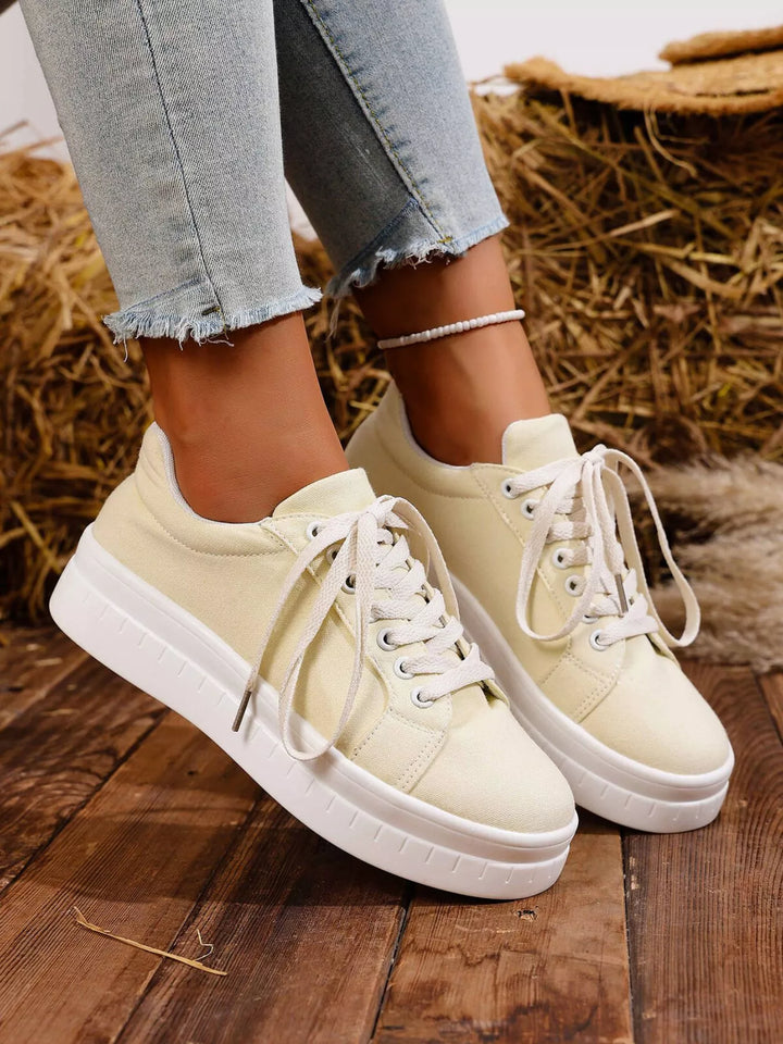 Cream low top lace up sneakers worn with raw hem jeans, angled view