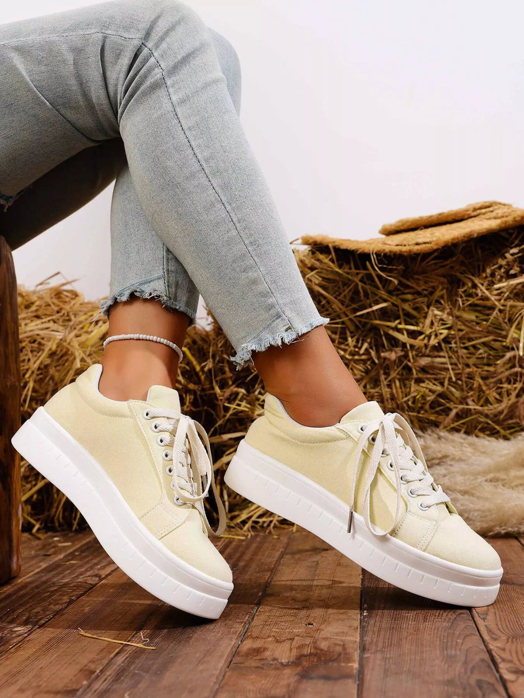 Cream chunky sole sneakers with crossed legs against hay bales