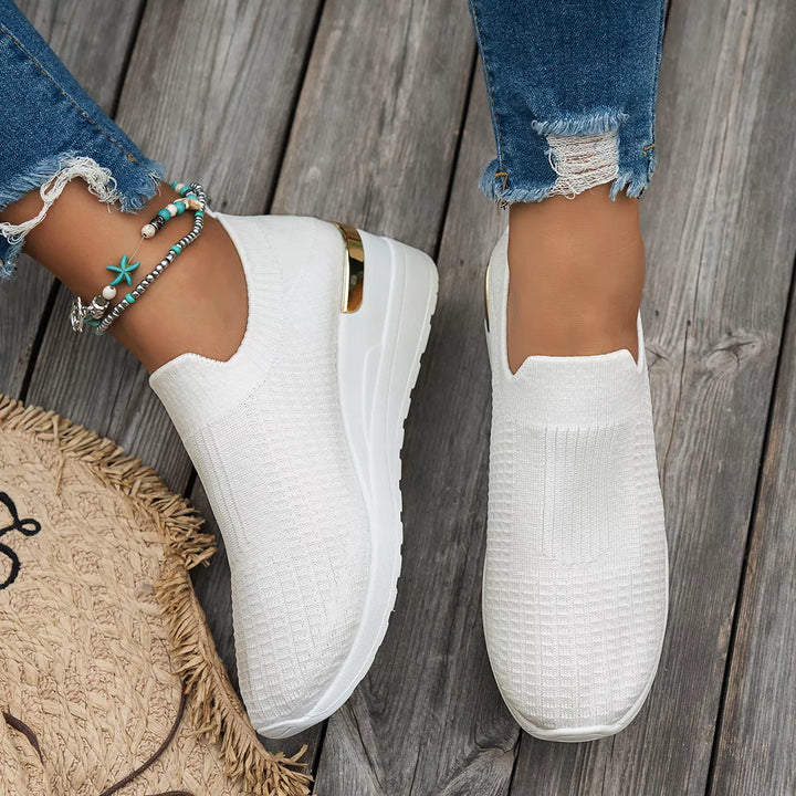 White slip on platform sneakers worn with ankle bracelets, front view