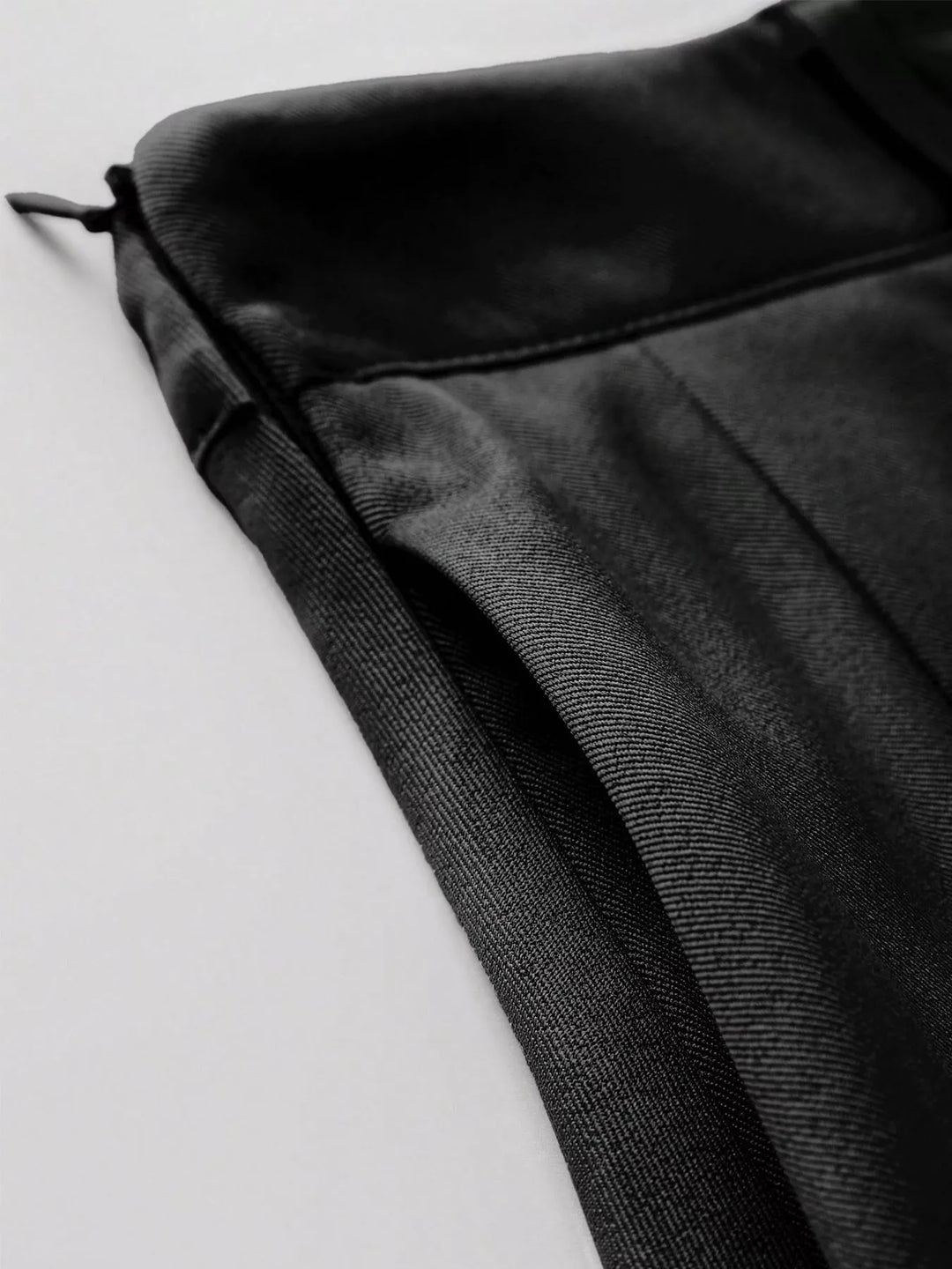 Close-up of the black pleated mini skirt waistband and side tie detail