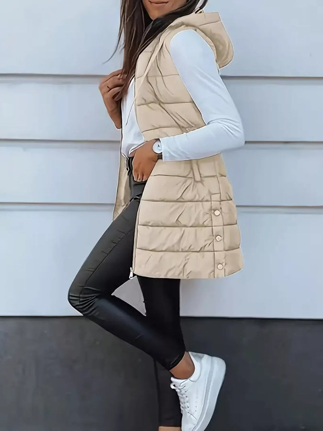 Side pose in the beige hooded puffer vest with white sneakers