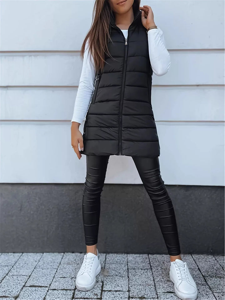 Full-length black quilted vest zipped up with black pants and white sneakers