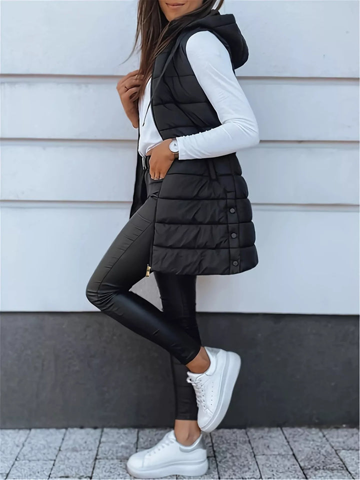Side pose in the black longline quilted vest with white sneakers
