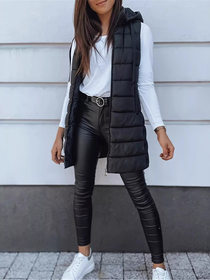 Black hooded puffer vest worn open, styled with leather pants and a white top