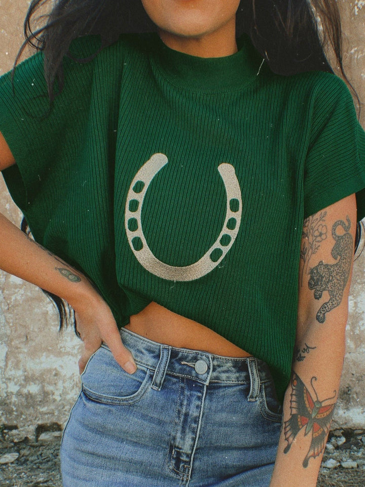 Women's short sleeve sweater in dark green, cropped with a horseshoe graphic, worn with jeans