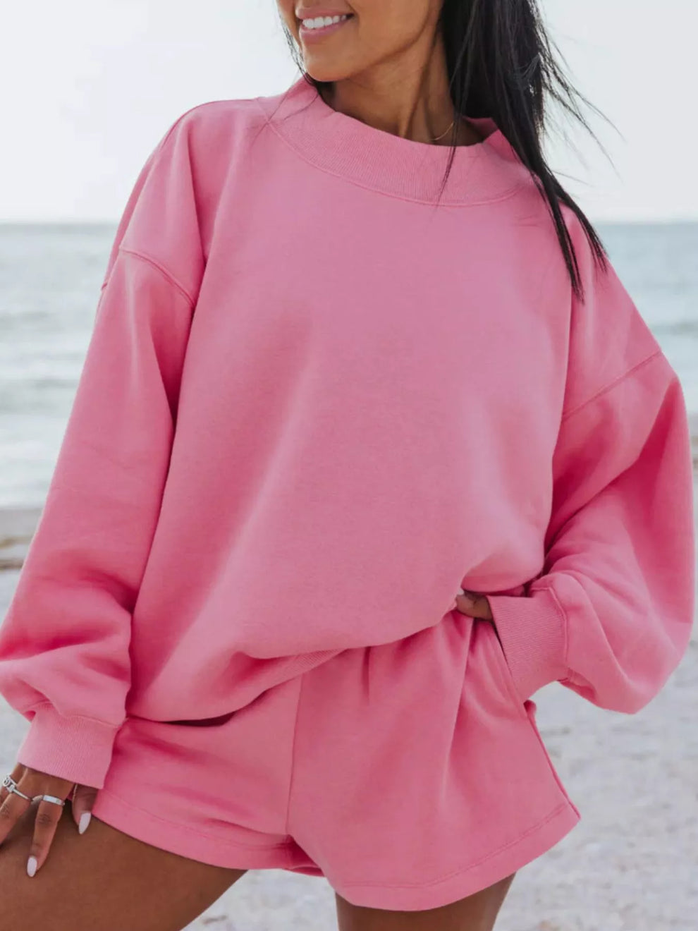 Hot pink sweatshirt and shorts set, hand on hip, standing by the water