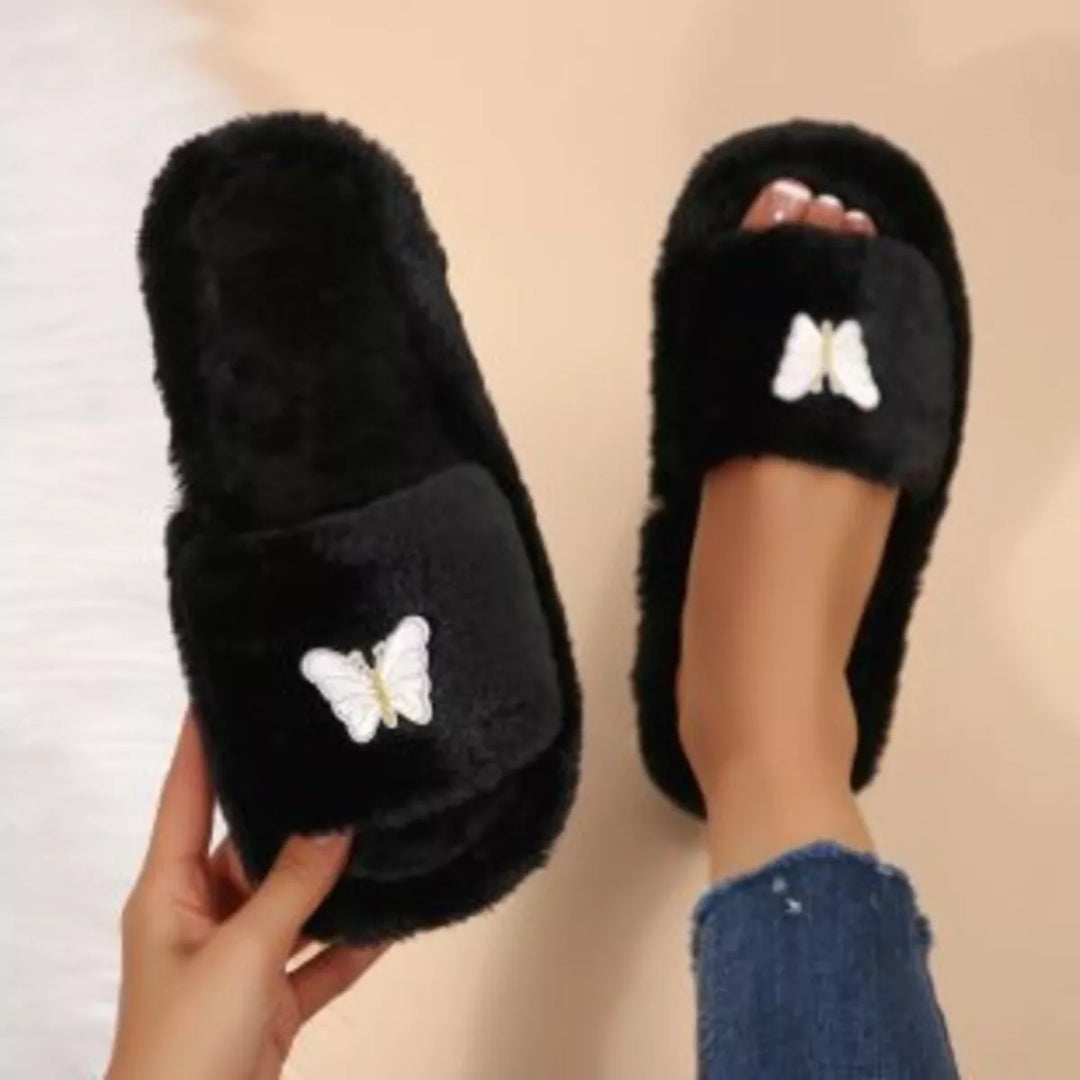 Black fluffy butterfly slippers held in hand, top view of one worn
