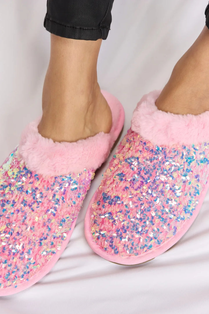 Close-up of pink sequin slippers and plush collars on feet