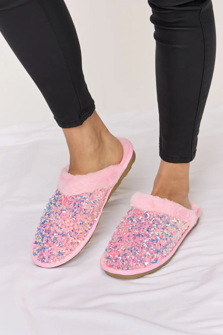 Pair of pink sequin slippers with plush collars, worn with black pants