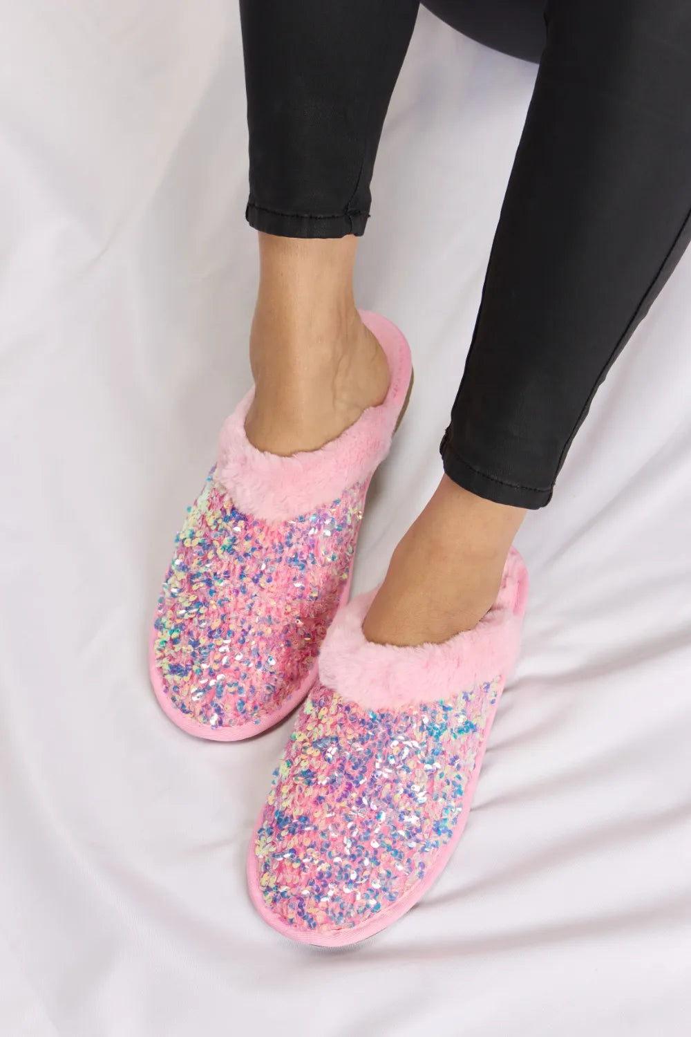 Women's slippers in pink with sequins and plush collar, worn with black leggings