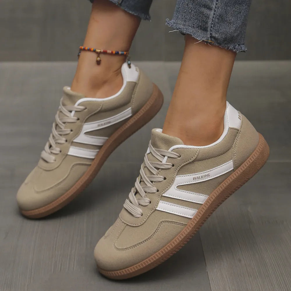Sand colored retro low top sneakers with white contrast stripes, worn with jeans