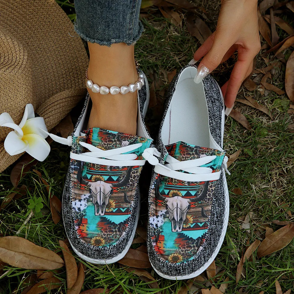 Gray bull print slip on sneakers with turquoise accents on a grassy background