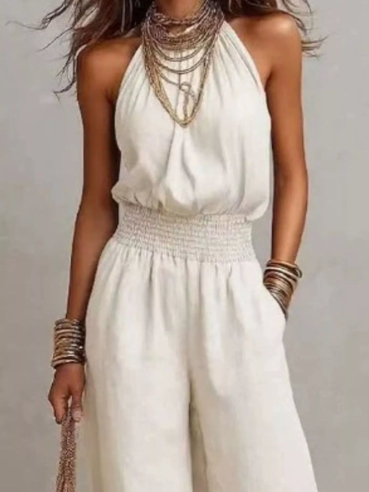 White halter neck jumpsuit, close view of the smocked waist and layered necklaces
