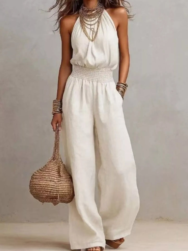 Women's summer jumpsuit in white with halter neck and wide leg, carried with a straw bag