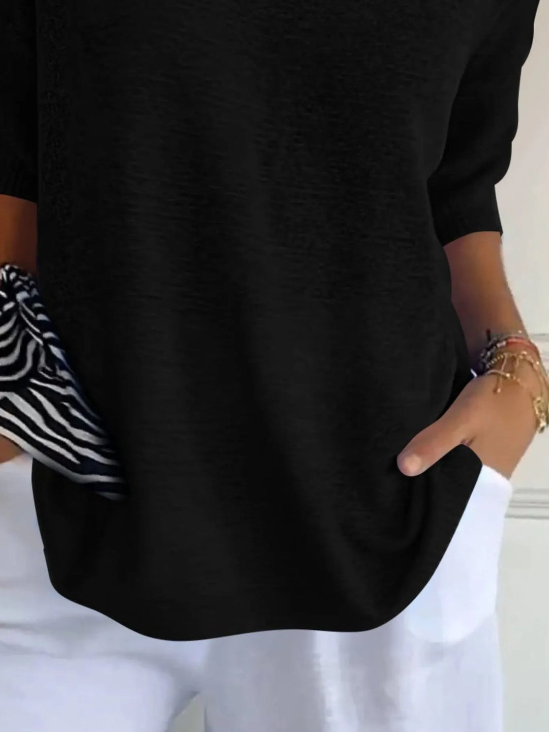 Black sweater detail of the 3/4 sleeve and hem, hand in pocket
