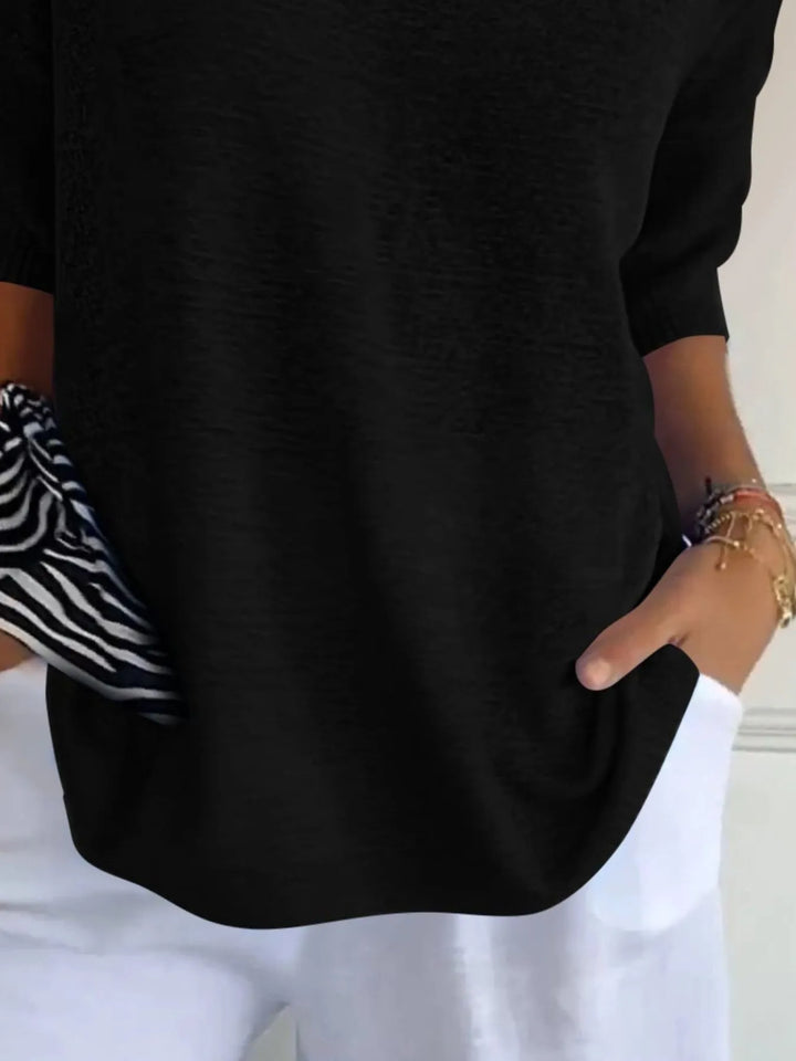 Black sweater detail of the 3/4 sleeve and hem, hand in pocket