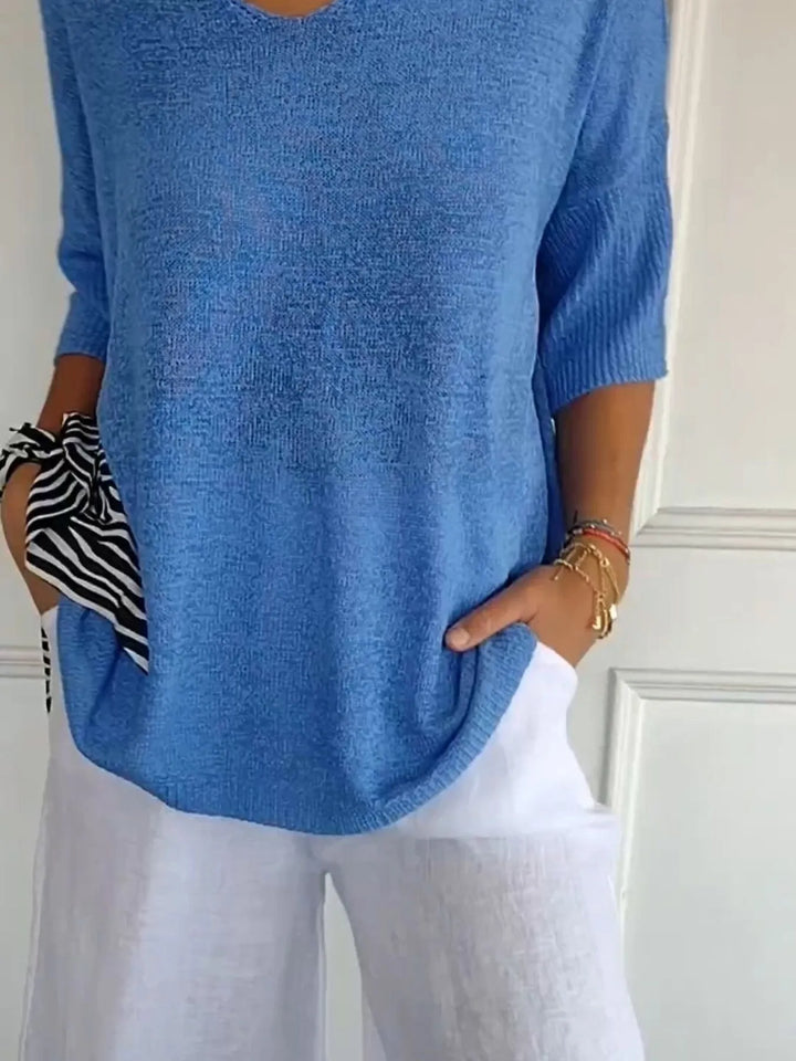 Blue V neck sweater with 3/4 sleeves, worn with white pants and a scarf
