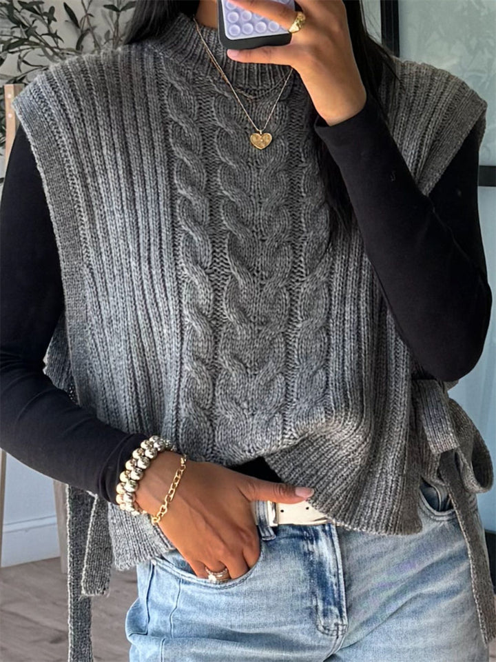 Gray cable knit vest worn over a black long sleeve top and jeans