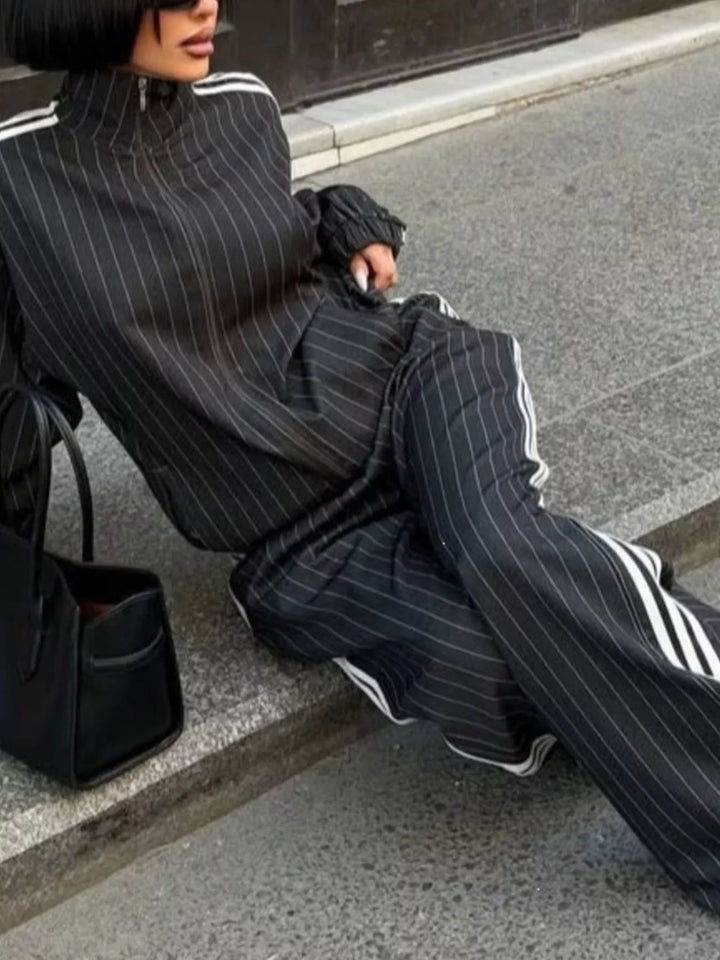 Black pinstripe tracksuit set worn while sitting on a curb with a black bag
