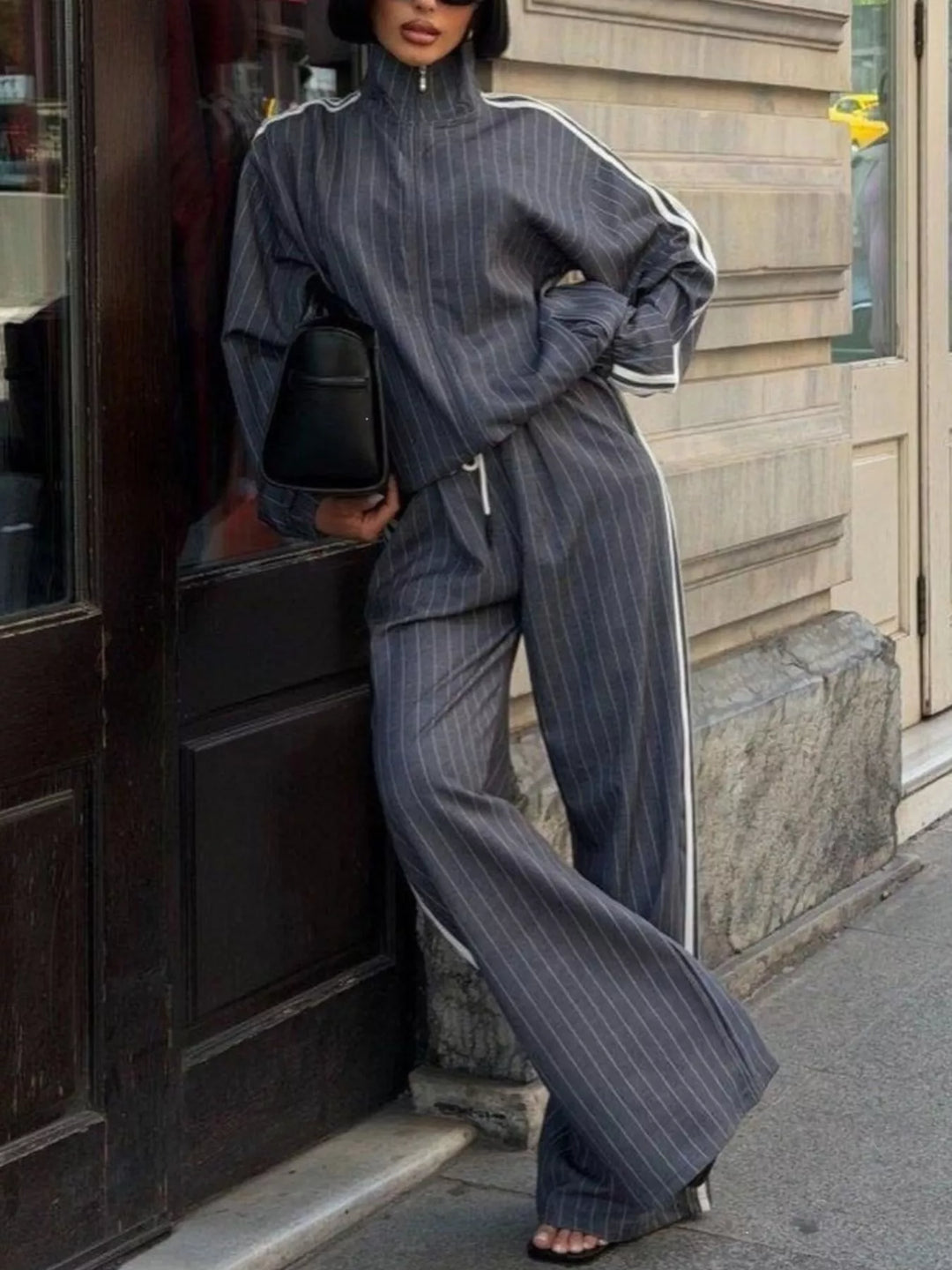 Gray pinstripe tracksuit with white side stripes, leaning against a stone wall
