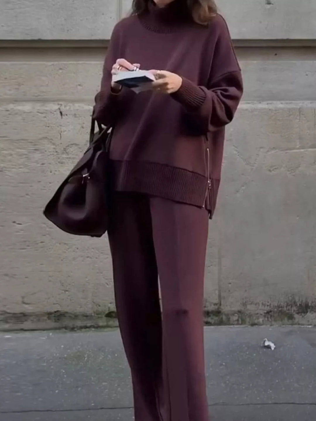 Burgundy mock neck pullover and wide leg pants, standing with a handbag and book