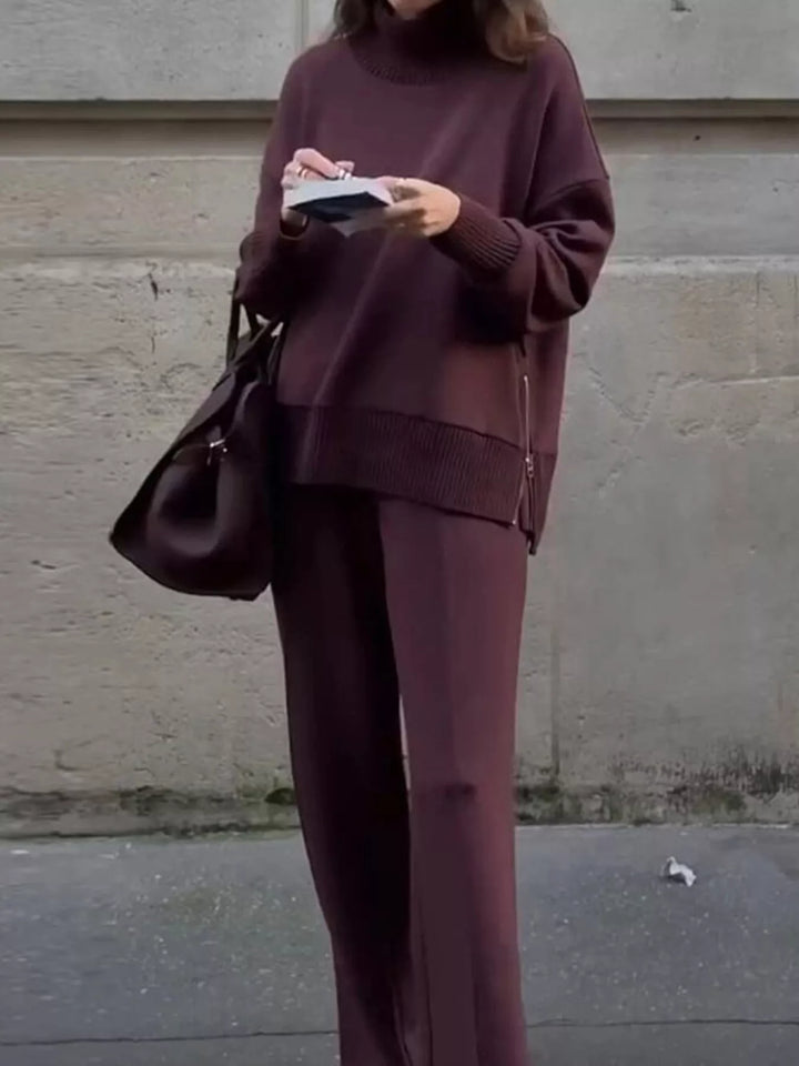 Burgundy mock neck pullover and wide leg pants, standing with a handbag and book