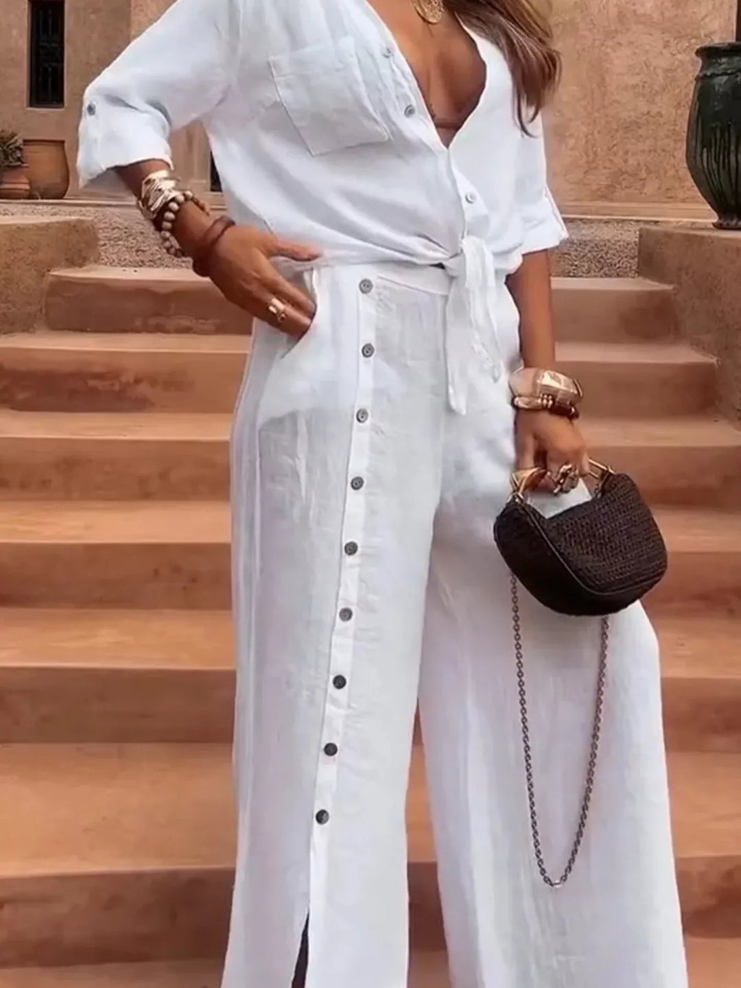 White tie front shirt and wide leg pants, hand on hip, holding a chain strap bag