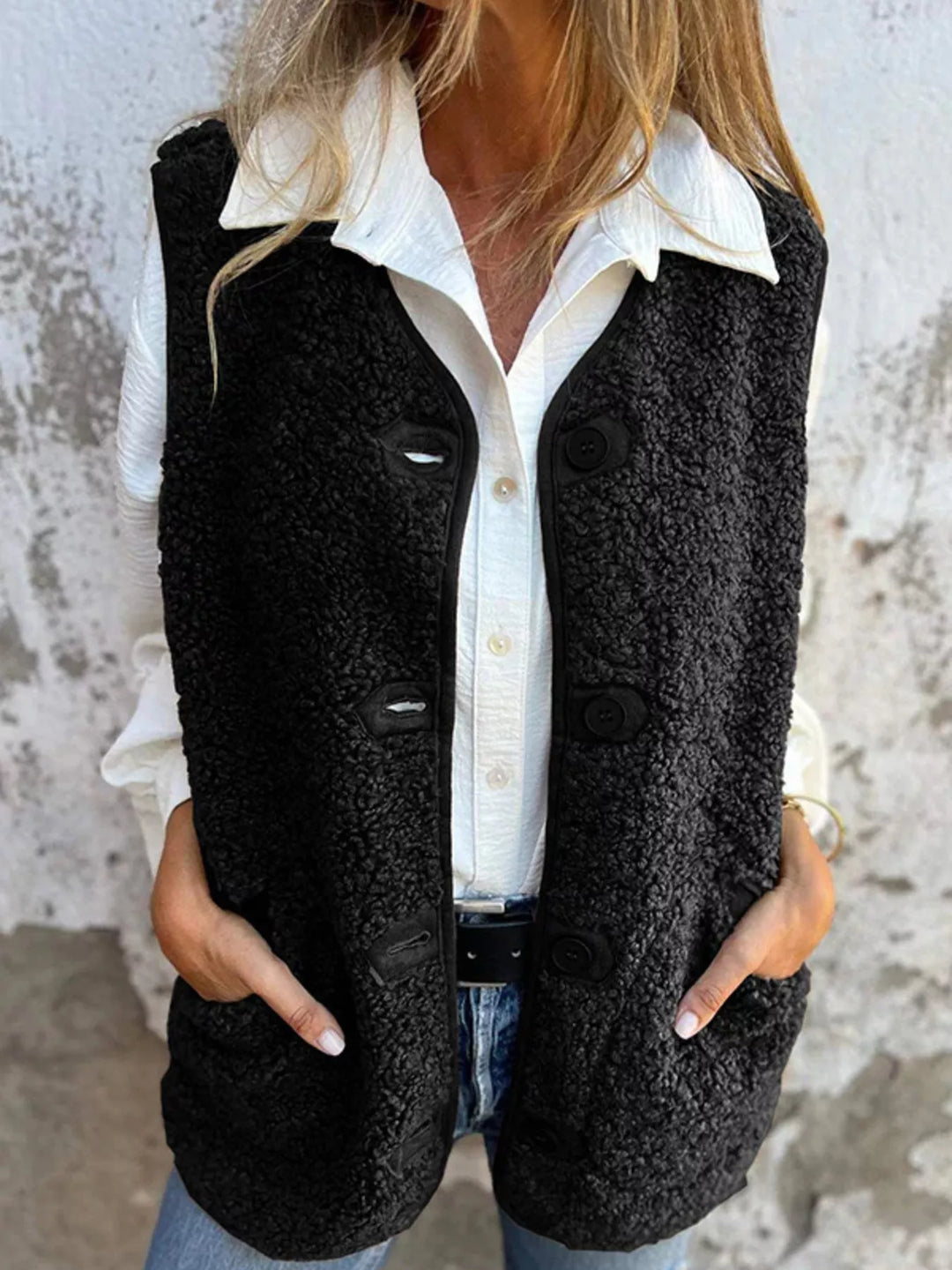 Black fluffy sleeveless vest with button front over a white collared shirt and jeans