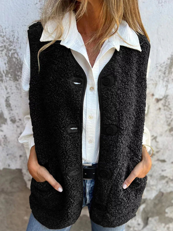 Black fluffy sleeveless vest with button front over a white collared shirt and jeans
