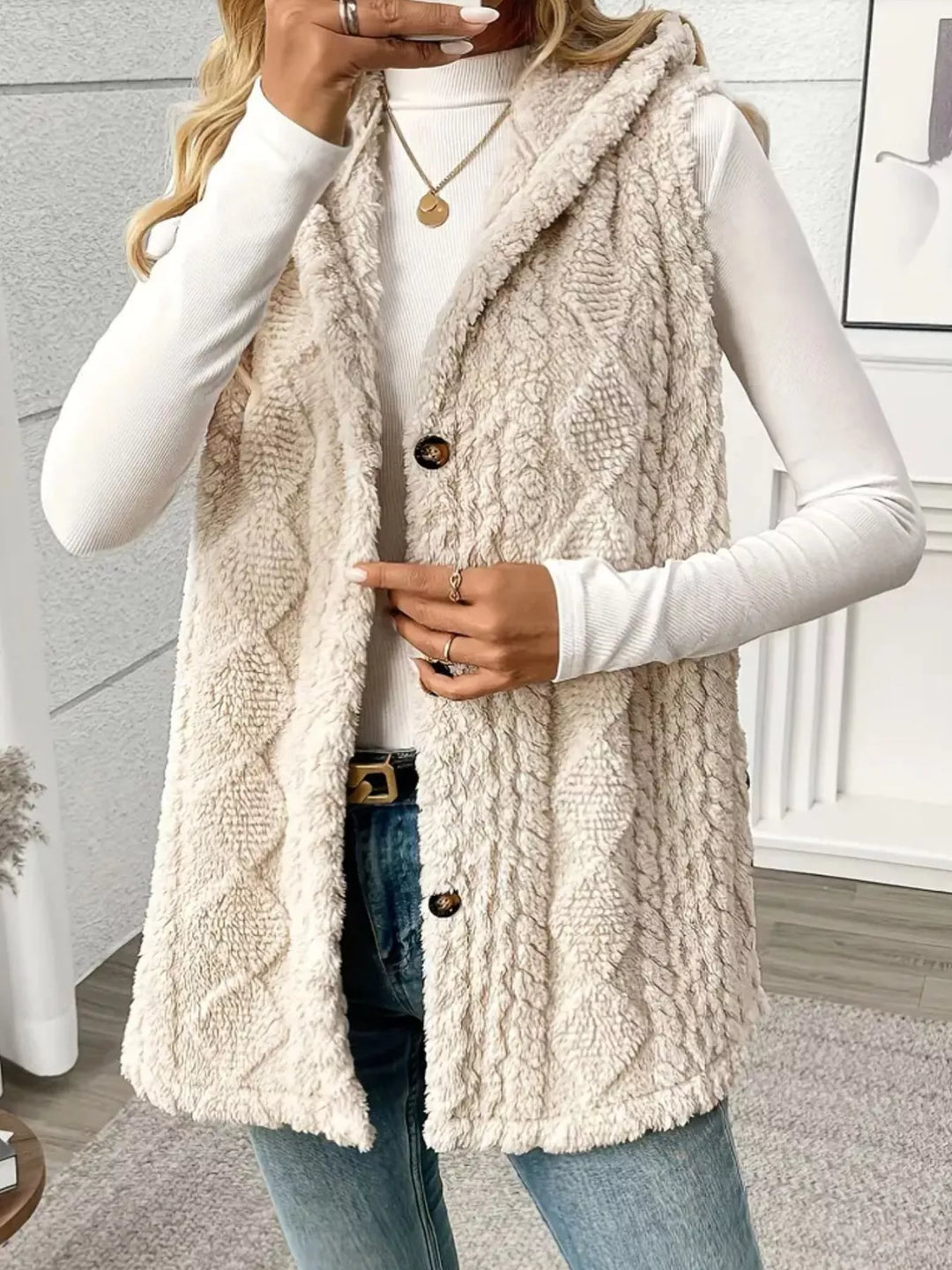 Beige fuzzy cable knit vest buttoned at the waist with jeans and a belt