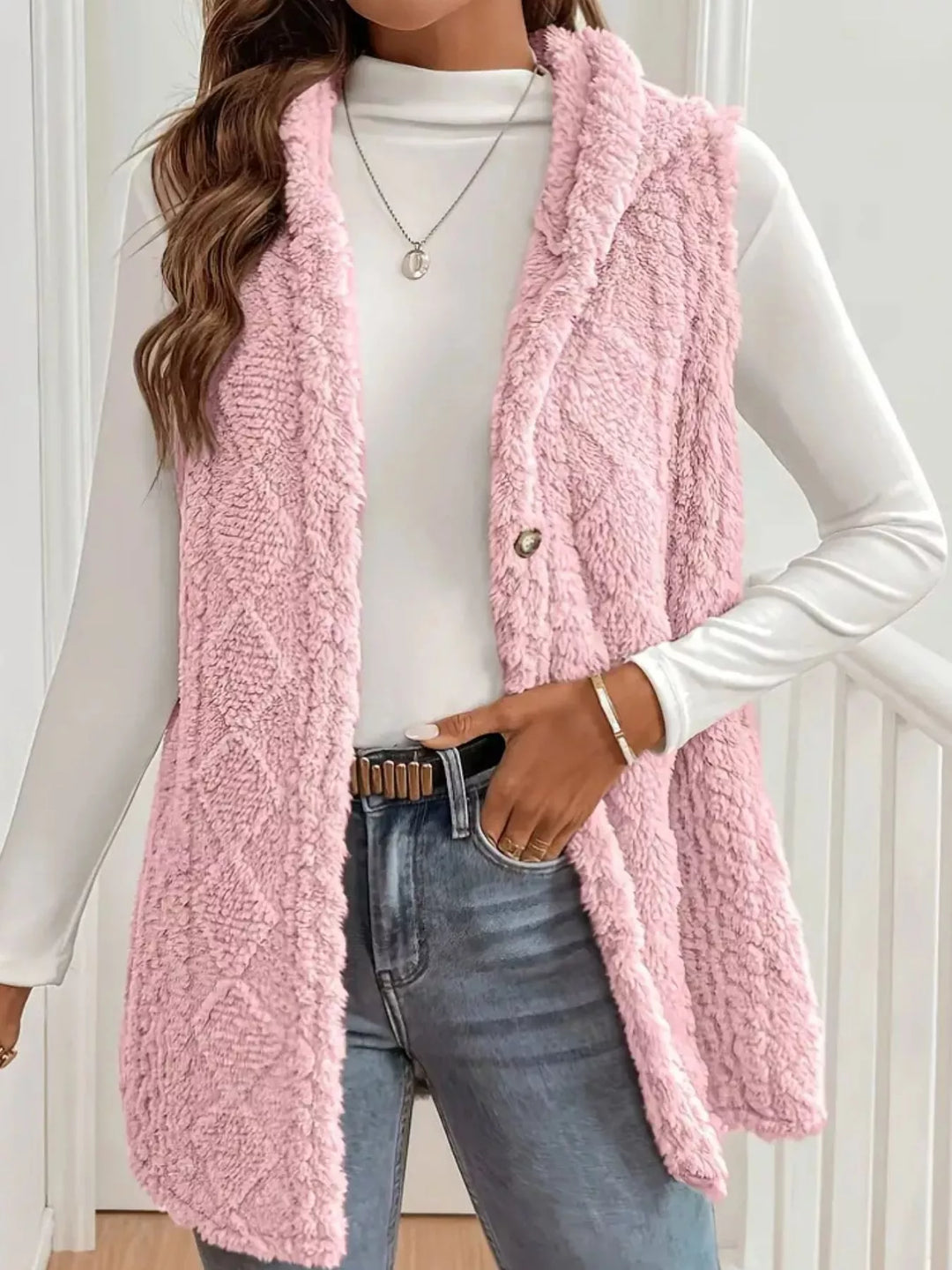Blush pink hooded fuzzy cable knit vest worn open with jeans and a belt