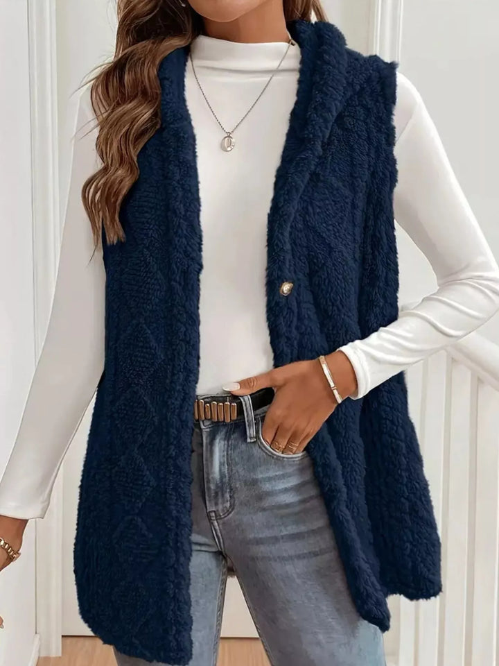 Navy hooded fuzzy cable knit vest worn open over a white mock neck top